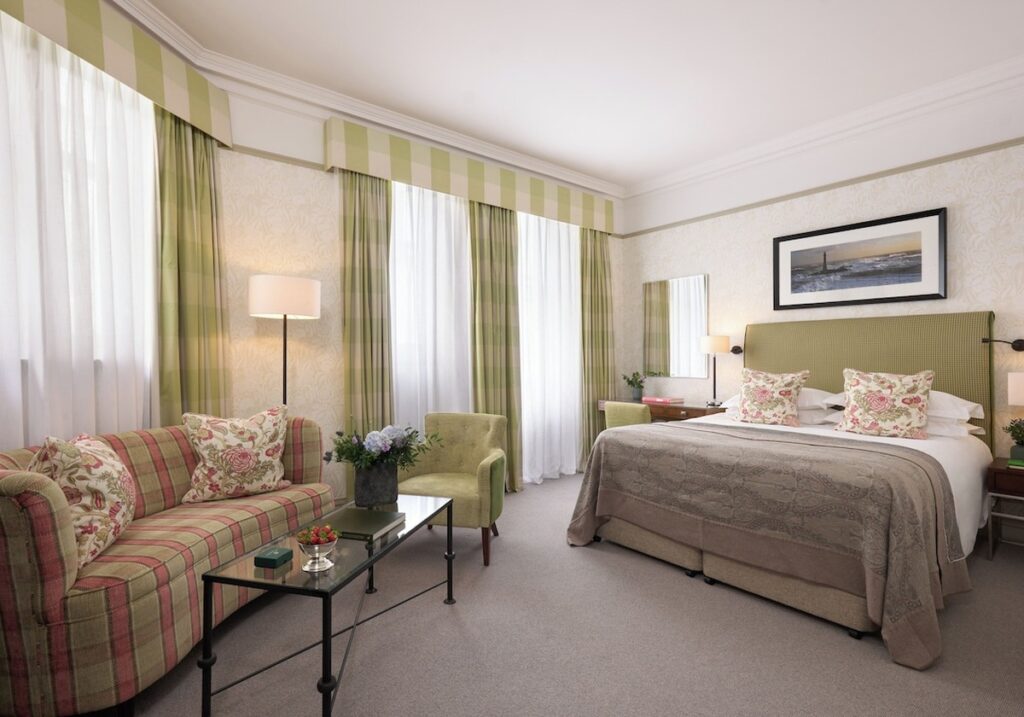 Quarto Classic do Balmoral hotel decorado em tons de verde sálvia e rosa, com sofá em xadrez tartã e cabeceira estofada com textura.