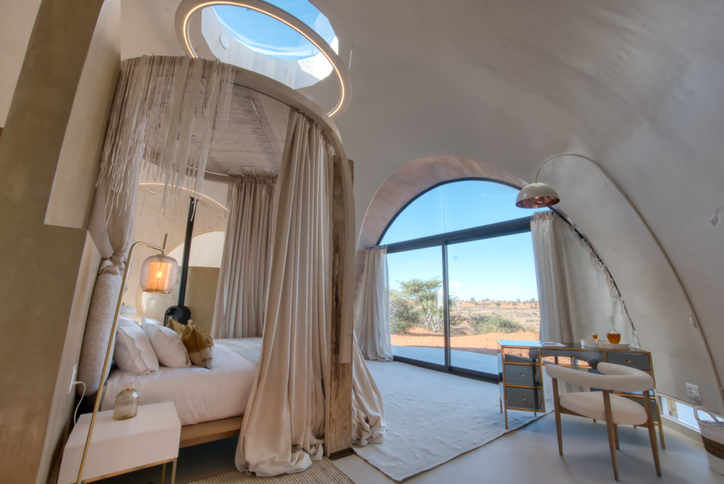 Quarto sob cúpula orgânica com dossel circular e claraboia zenital no Reverie Kalahari Pod, integrado às dunas.