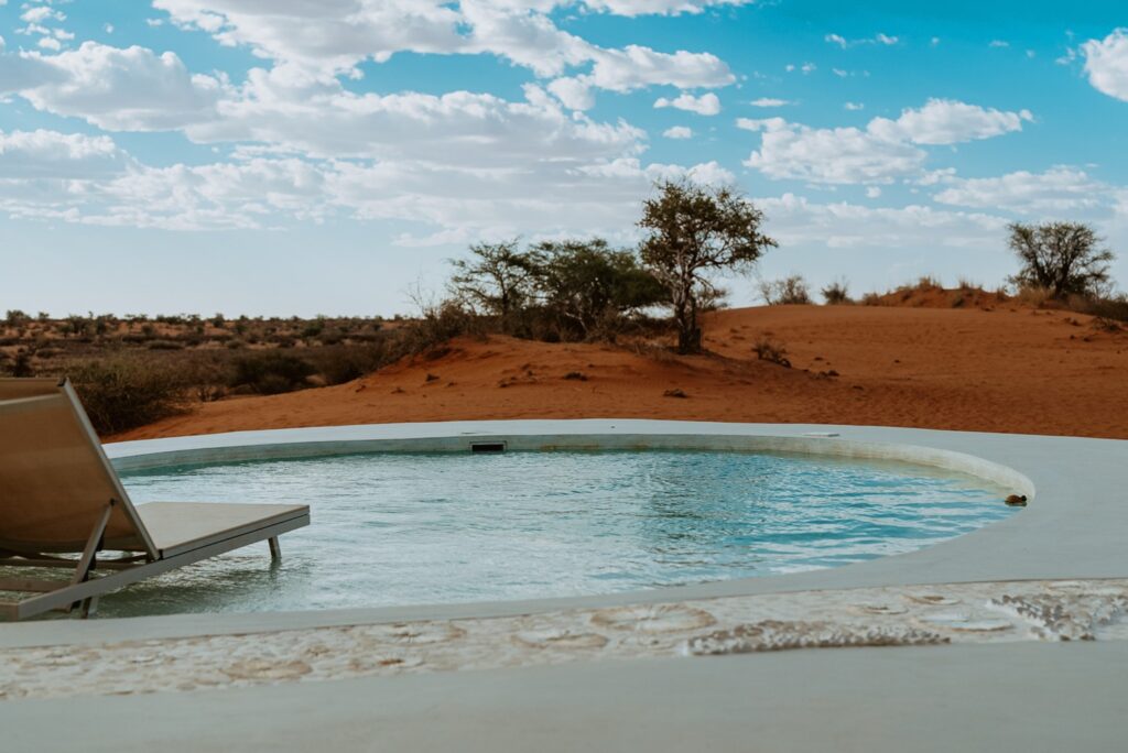 Piscina de mergulho curva integrada às dunas avermelhadas em exclusivo retiro no deserto com espreguiçadeira na água.