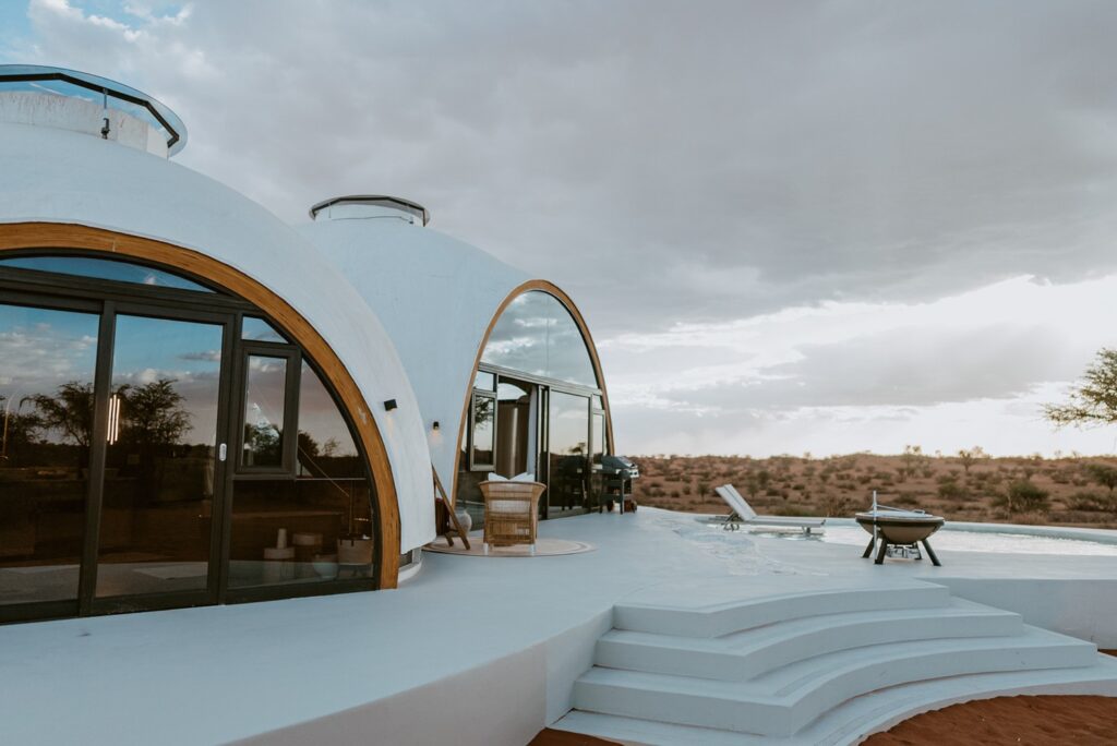 Arquitetura dos domos brancos interconectados com deck curvo e piscina no Reverie Kalahari Pod ao entardecer.