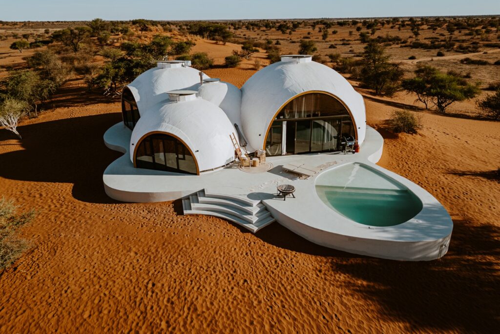 Vista aérea dos domos brancos integrados ao solo arenoso e deck biomórfico do Reverie Kalahari Pod na Namíbia.