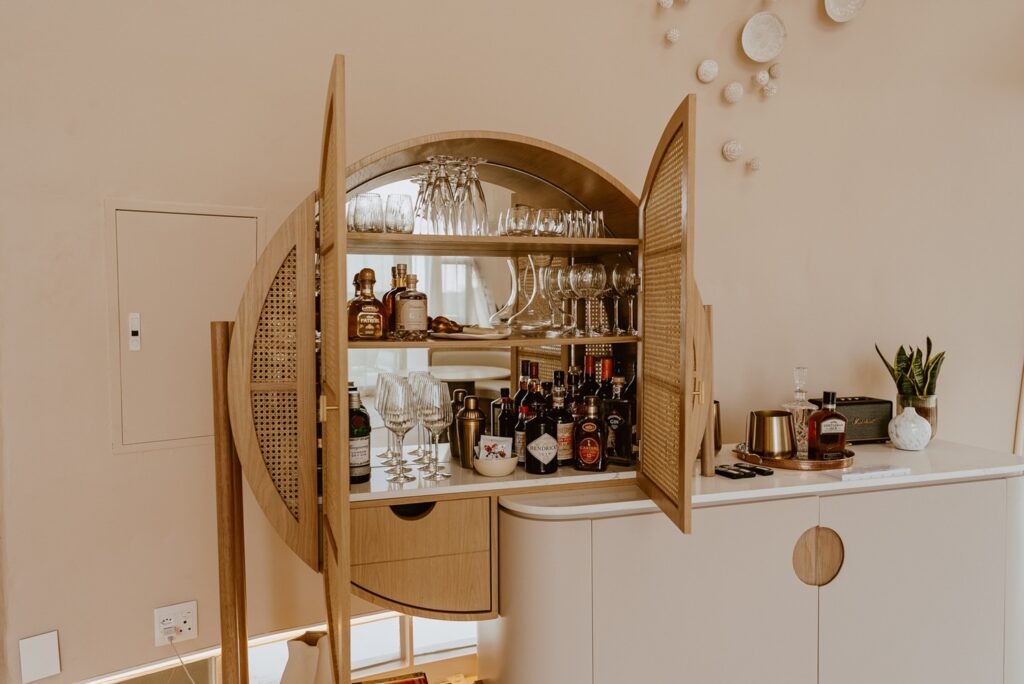 Armário bar artesanal em marcenaria curva com portas em palhinha e seleção de destilados no Reverie Kalahari Pod.
