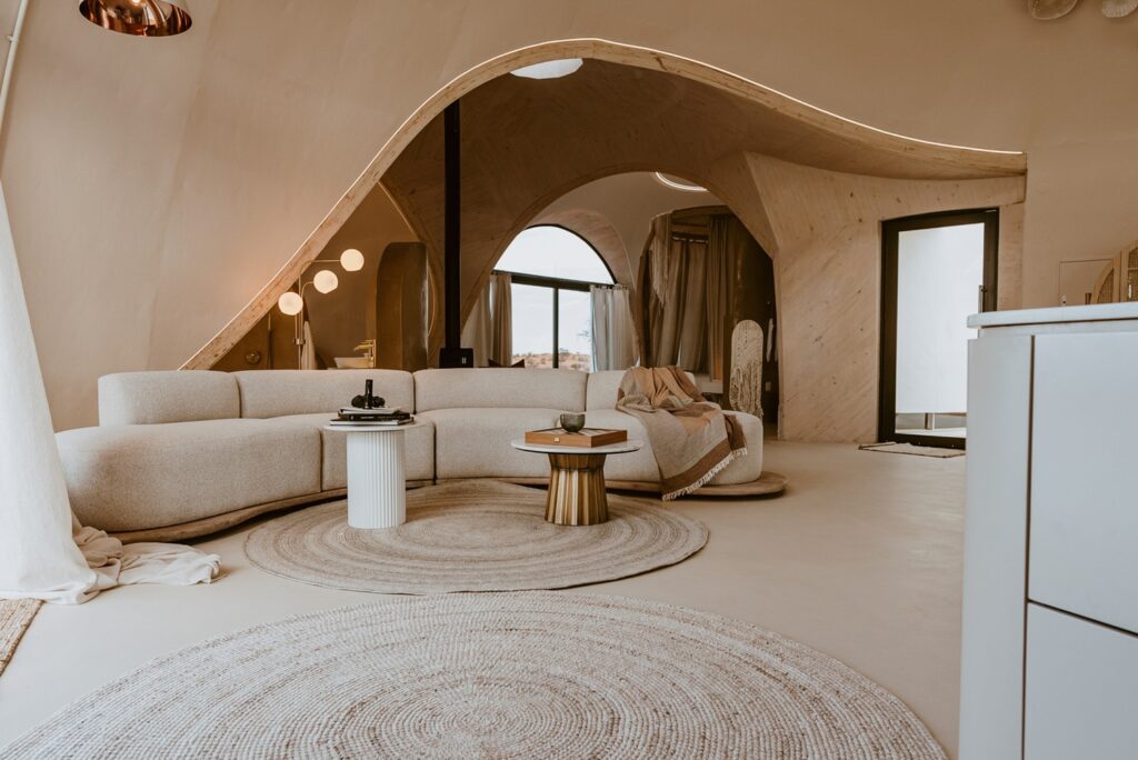 Living com sofá curvo em bouclé e arcos esculturais em madeira laminada integrando os domos do Reverie Kalahari Pod.