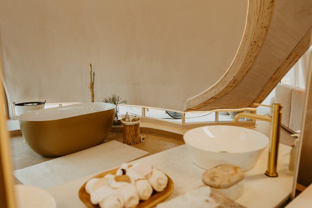 Sala de banho integrada com banheira oval dourada e metais em latão escovado no exclusivo Reverie Kalahari Pod.