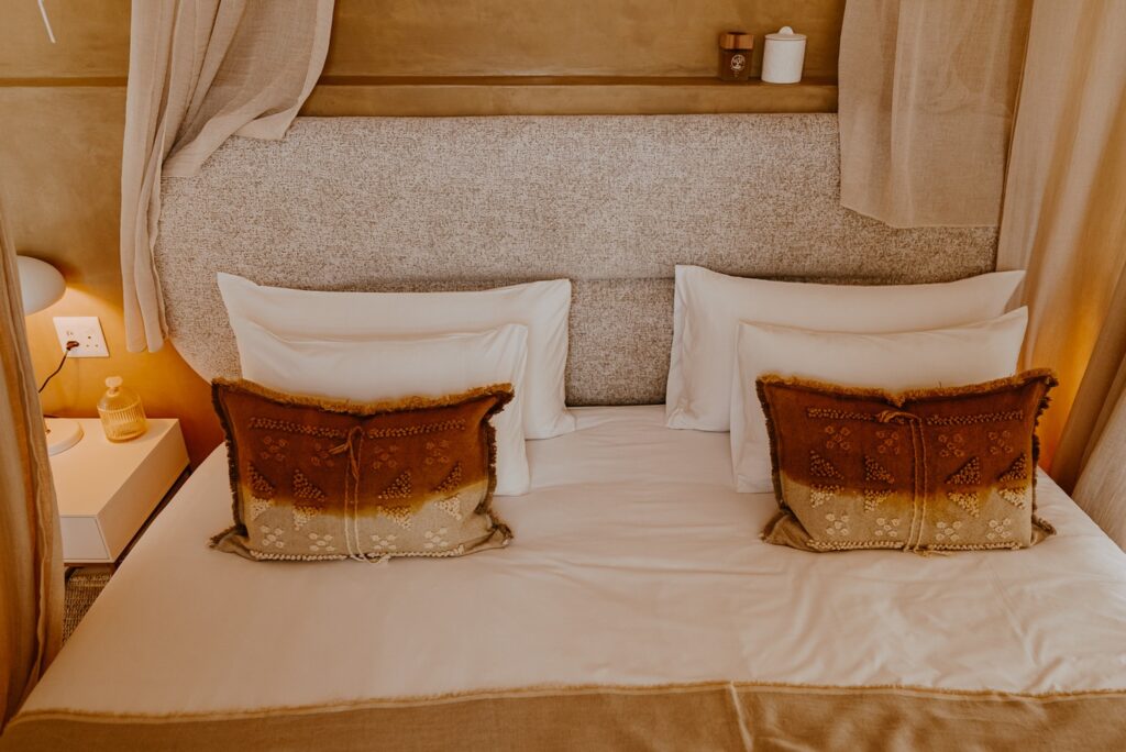 Detalhe da cama king-size com cabeceira estofada e almofadas artesanais em terracota no Reverie Kalahari Pod.