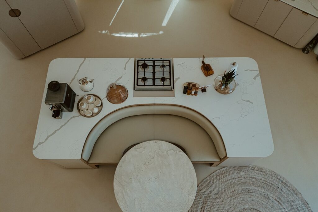 Visão superior da ilha com cooktop e canto alemão integrado à mesa de jantar circular em retiro no deserto.