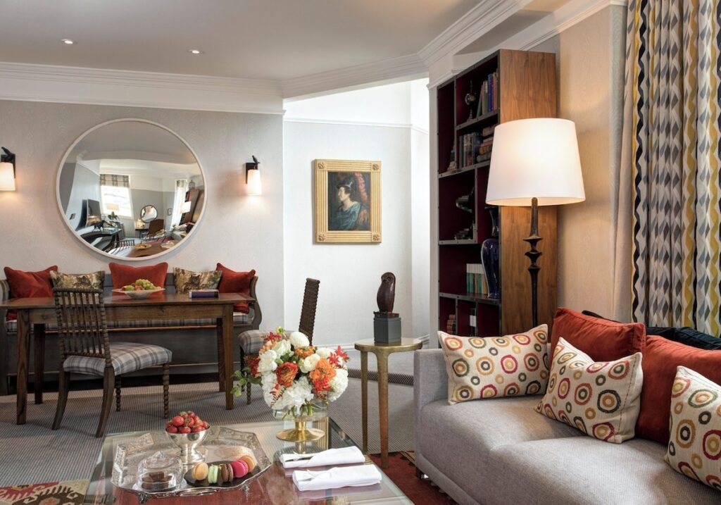 Sala de estar da Suíte J.K. Rowling no Balmoral hotel com estante em carvalho, espelho circular, detalhes em terracota e mesa de jantar.