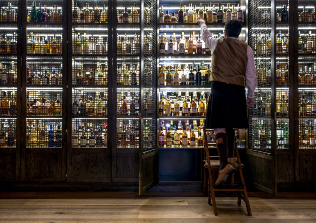 Bar SCOTCH no Balmoral hotel com estante iluminada do chão ao teto exibindo coleção de whiskies escoceses em nichos retroiluminados.