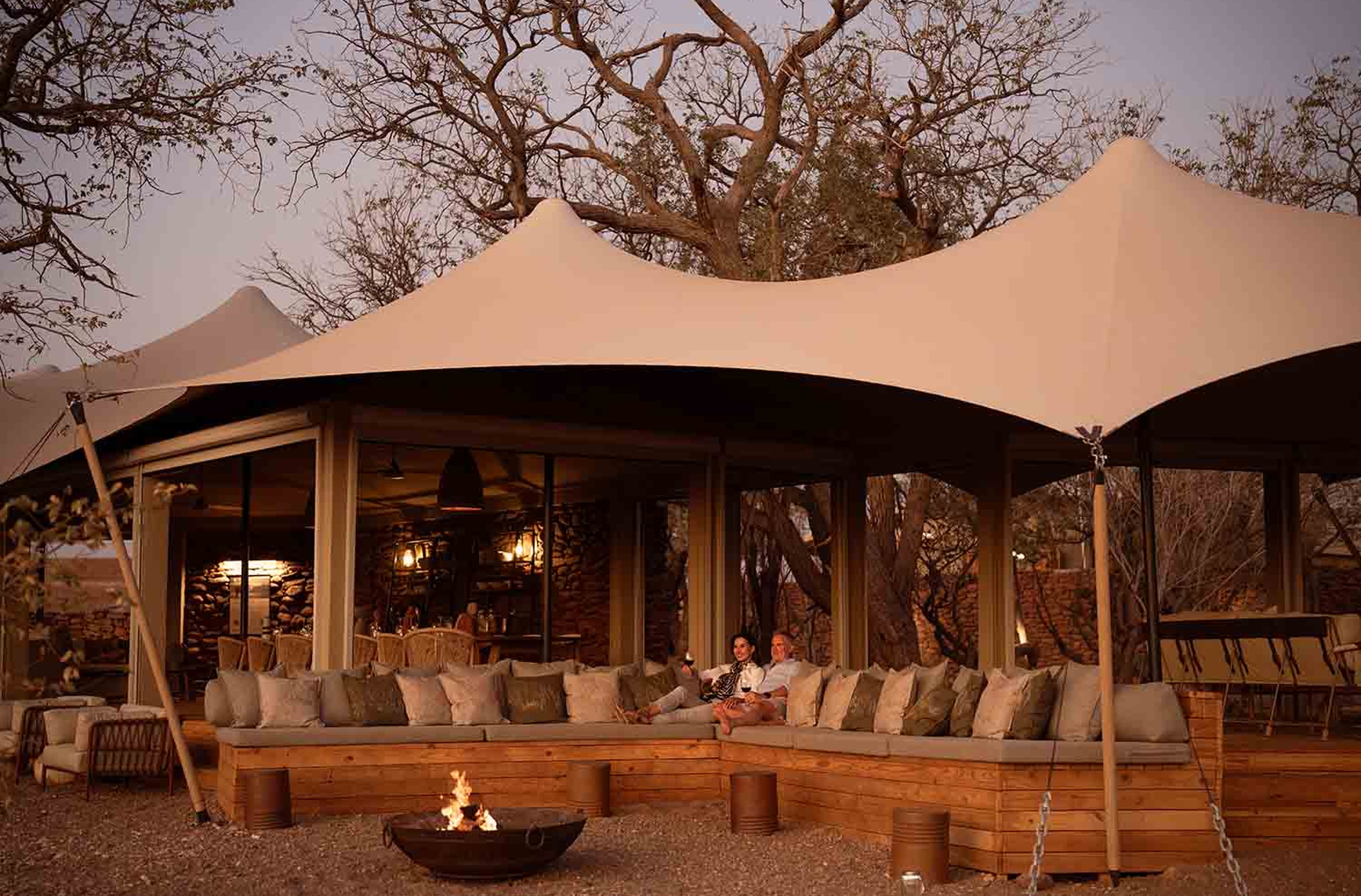 Deck lounge ao ar livre com fogueira e tenda tensionada no Desert Rhino Camp.