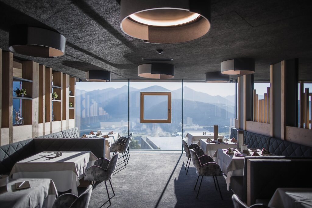 Restaurante panorâmico com janelões de vidro para as Dolomitas no Hotel Hubertus, sofisticação culinária em hotéis de luxo nos Alpes.