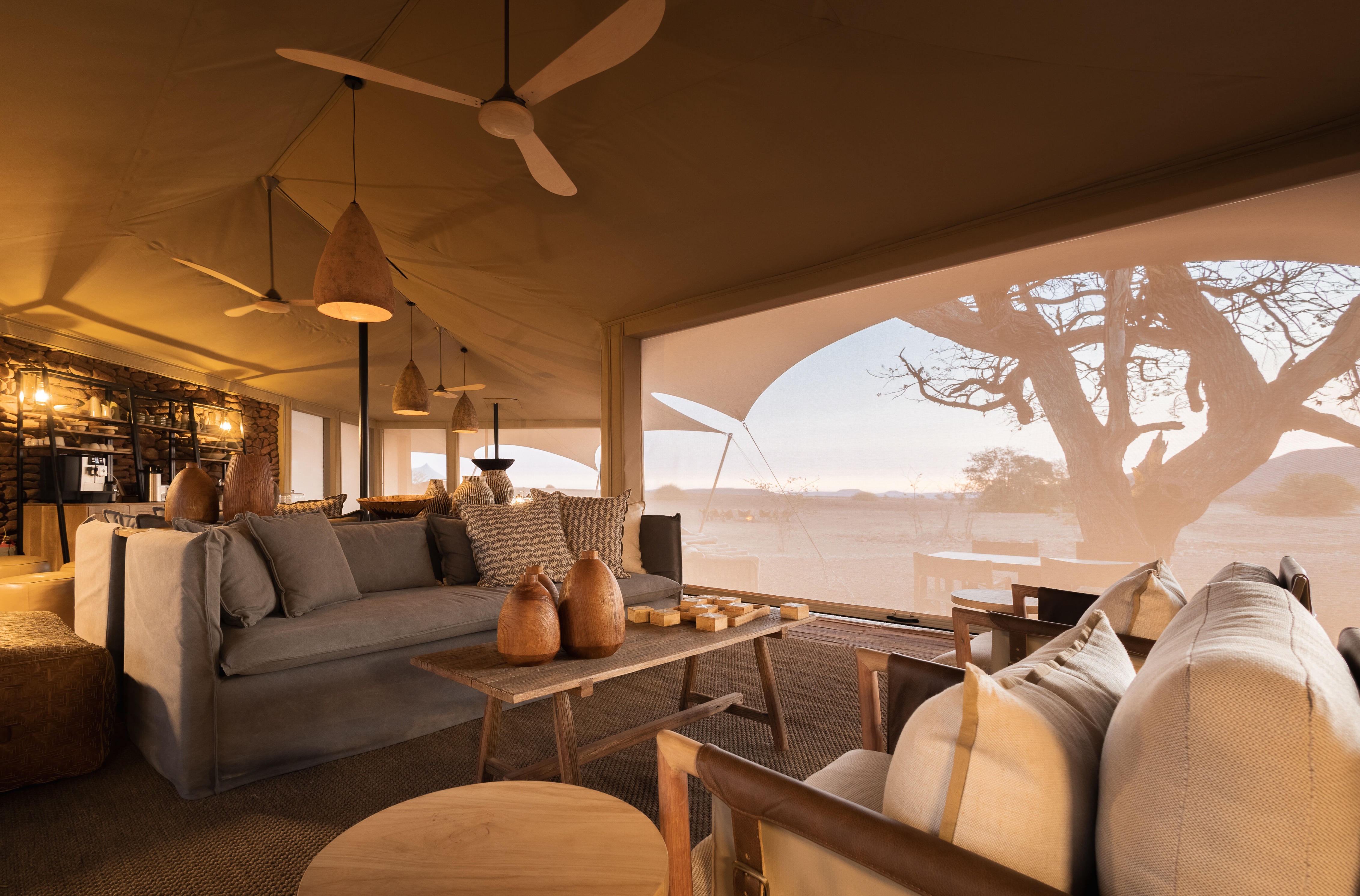 Lounge de estar interno com decoração terrosa e telas no Desert Rhino Camp.