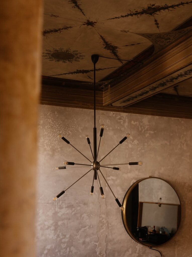 Lustre sputnik de latão sob teto decorado com afrescos no hotel G-Rough Roma.