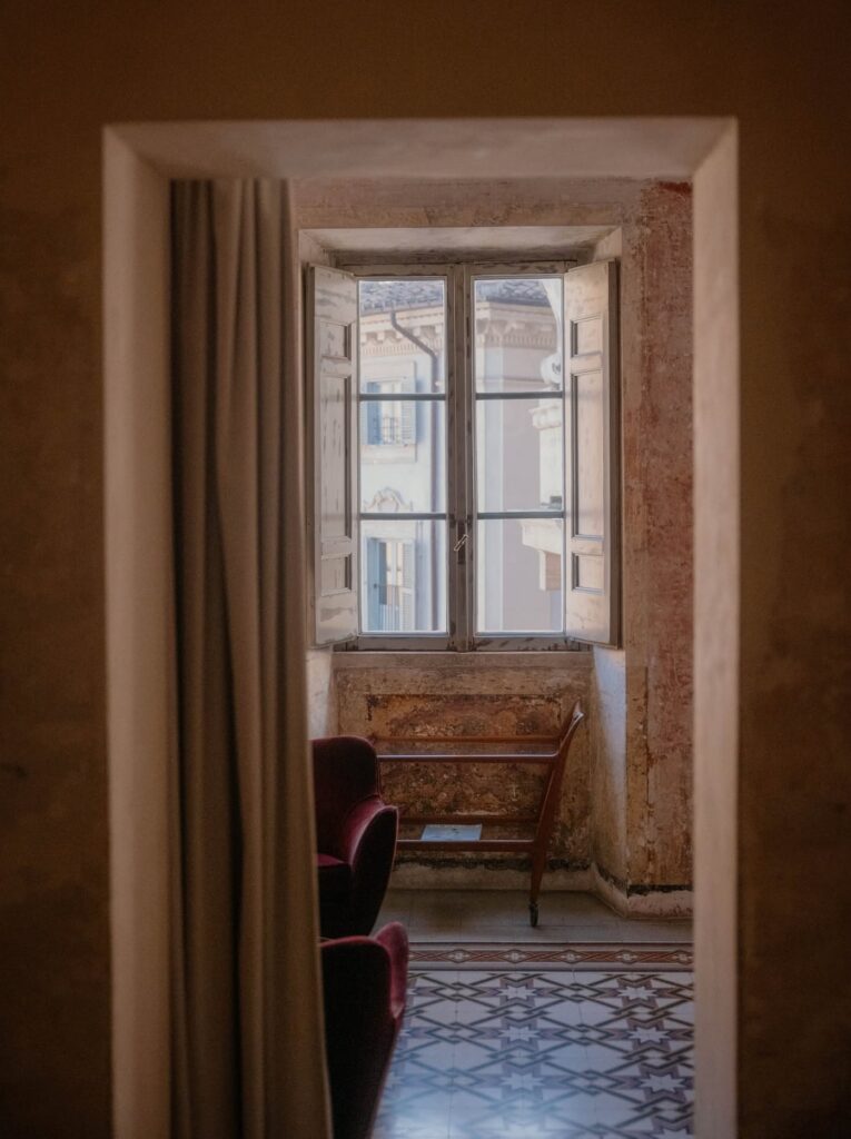 Janela clássica com venezianas de madeira e vista urbana no hotel boutique G-Rough Roma.