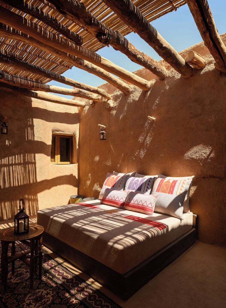 Daybed ao ar livre sob pérgola de palha com jogo de luz e sombra no Dar Tantora.