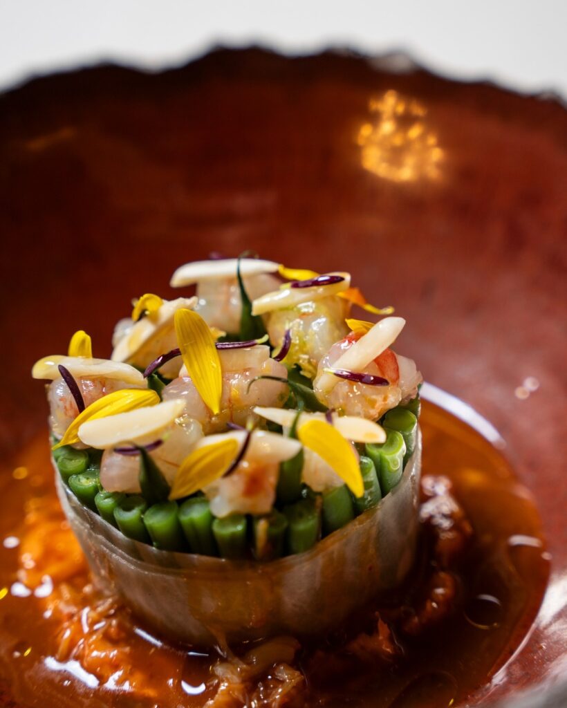 Prato de alta gastronomia da Osteria di Passignano em cerâmica terracota com frutos do mar, feijão-verde e pétalas comestíveis.