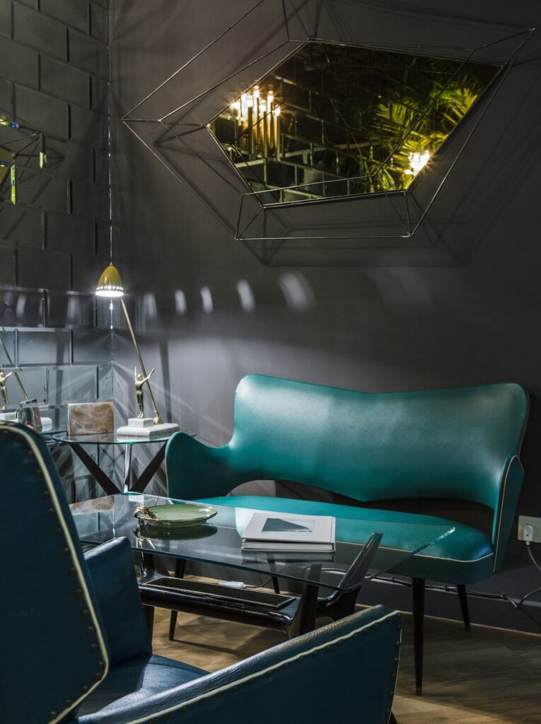 Saguão com sofá verde esmeralda e paredes escuras com espelhos no hotel boutique G-Rough Roma.