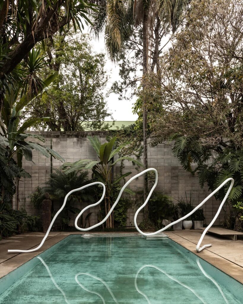 Escultura tubular branca sobre a piscina na Casa Ateliê Tomie Ohtake, museu pequeno em são paulo integrado a exuberante jardim tropical.