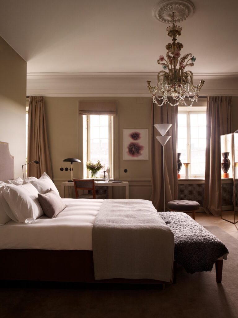 Suíte no hotel Ett Hem por Ilse Crawford com lustre de cristal Murano, paleta greige e iluminação natural.