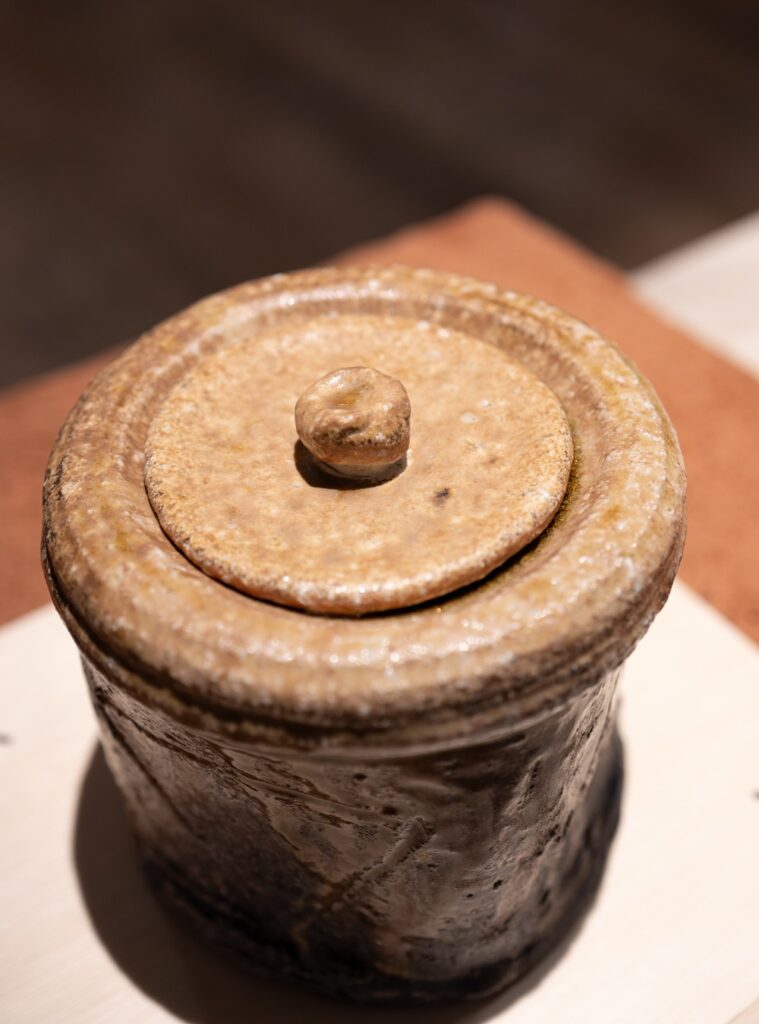 Pote cerâmico com tampa artesanal em suporte de madeira durante exposições em são paulo na Japan House.