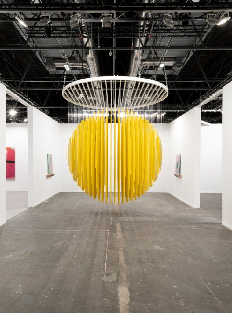 Esfera amarela cinética de Jesus Soto suspensa em exposição em São Paulo com ritmo visual e iluminação cênica na galeria.
