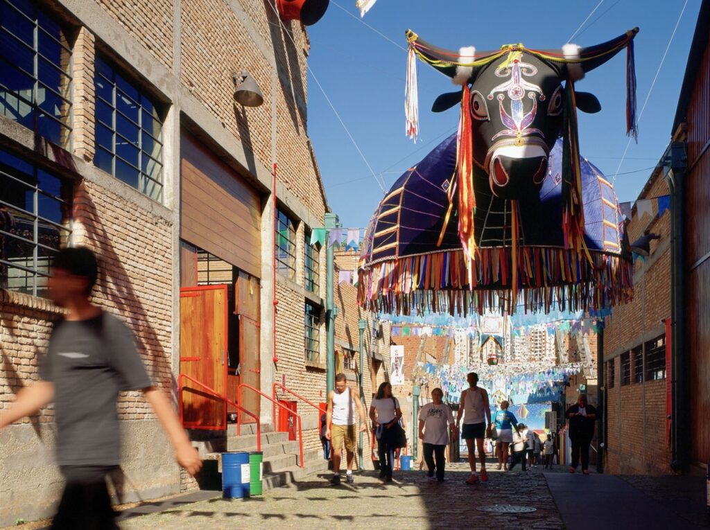 Rua interna com galpões de tijolo aparente e celebração cultural no SESC Pompeia, expoente do movimento brutalista.