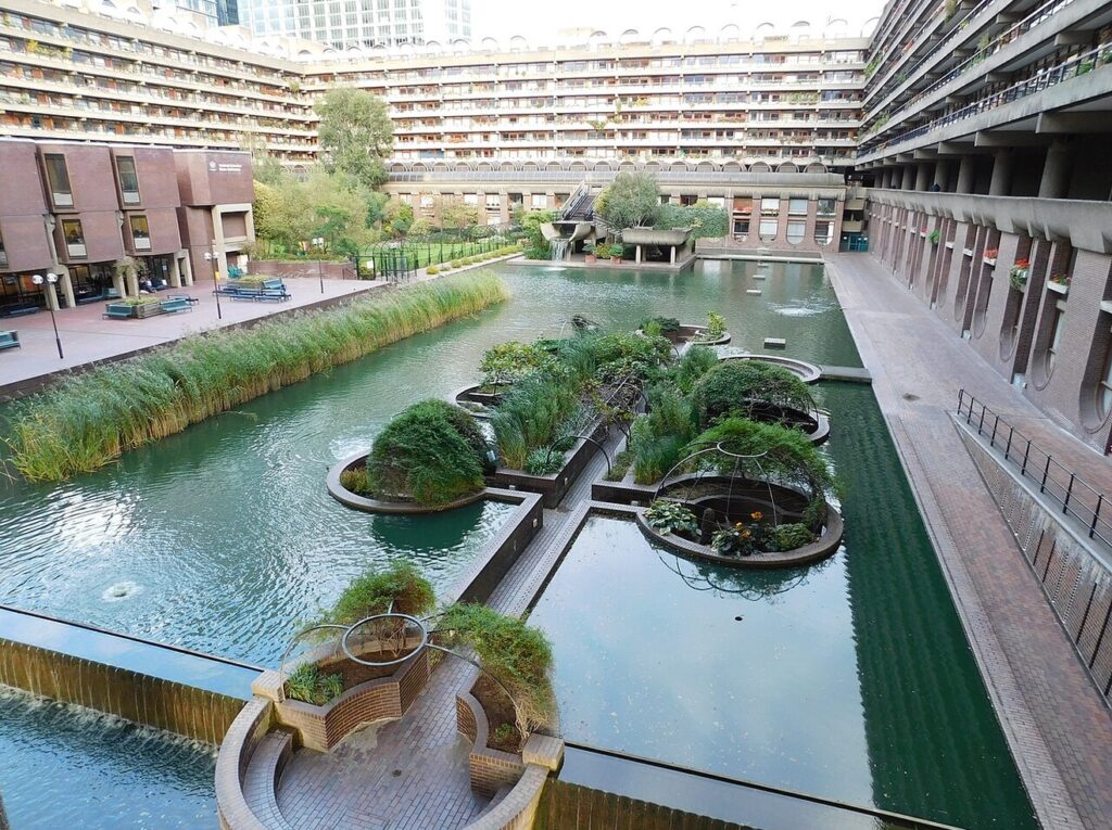 Vista aérea do espelho d'água e jardins integrados aos blocos residenciais do Barbican em Londres, marco do brutalismo.