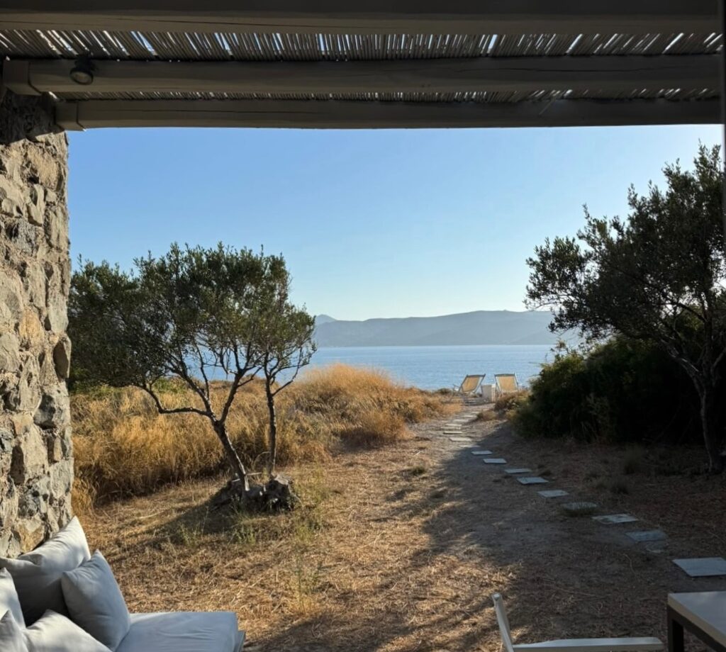 Varanda sombreada no Skinopi Lodge com forro de palha, vista para o Egeu e conexão direta com a paisagem natural das Syrmatas.