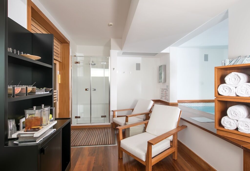 Área de spa e bem-estar no hotel Casa Angelina com poltronas em madeira, acabamentos em branco e vista para área relax.