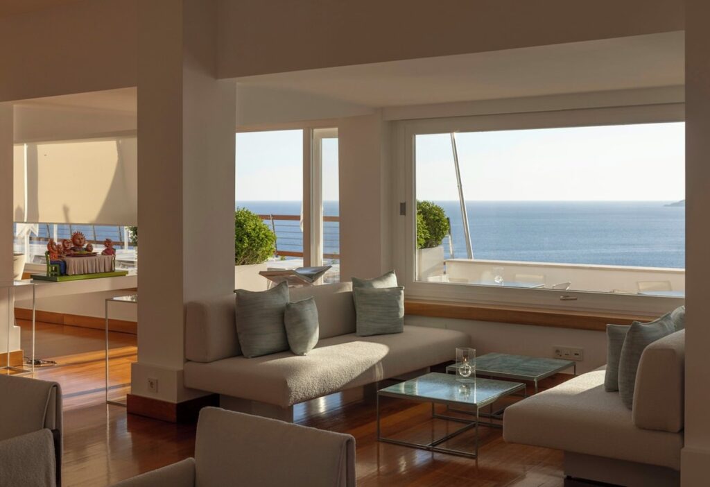 Ambiente de estar minimalista com sofás claros e ampla janela com vista marítima no hotel Casa Angelina.
