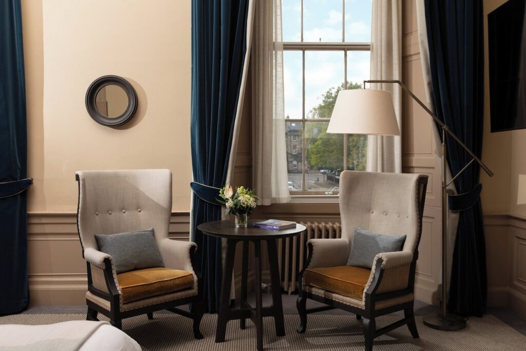 Poltronas de encosto alto e mesa bistrô junto à janela no Kimpton Charlotte Square.