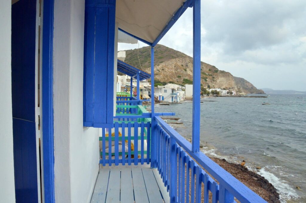 Varanda de Syrmatas na Blue Sea House em Milos com guarda-corpo azul cobalto, alvenaria caiada e vista panorâmica para o Mar Egeu.