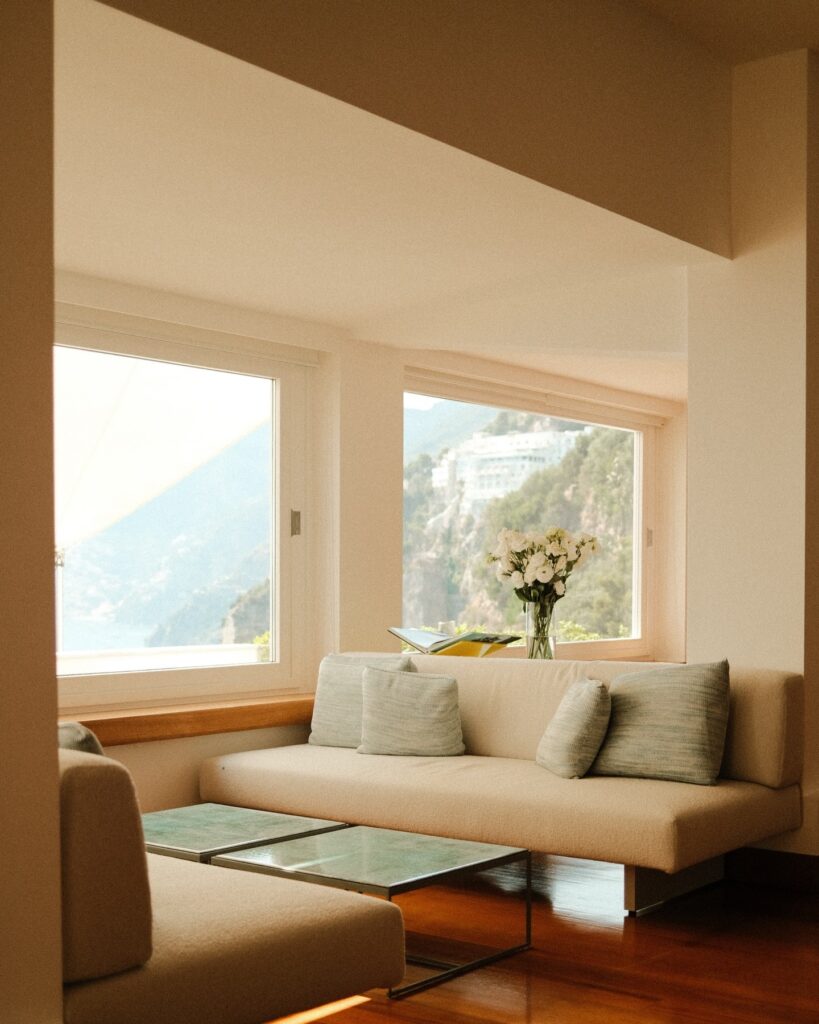 Sala de descanso com sofá neutro e janelas voltadas para as encostas de Positano no hotel Casa Angelina.