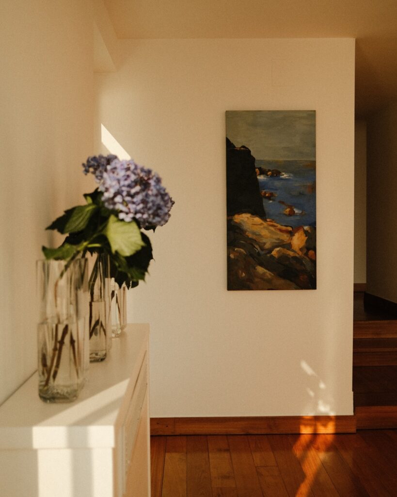 Aparador com flores e quadro de arte contemporânea sob iluminação suave no hotel Casa Angelina.