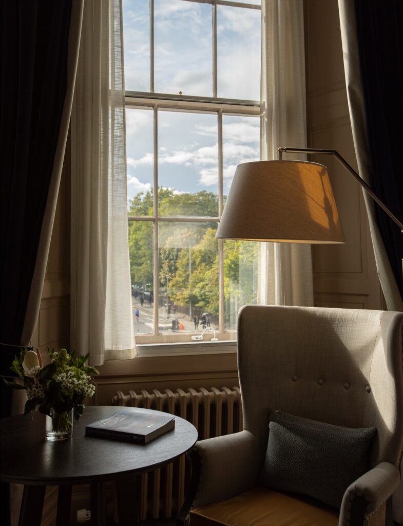 Canto de leitura com poltrona clássica e luz natural no Kimpton Charlotte Square.