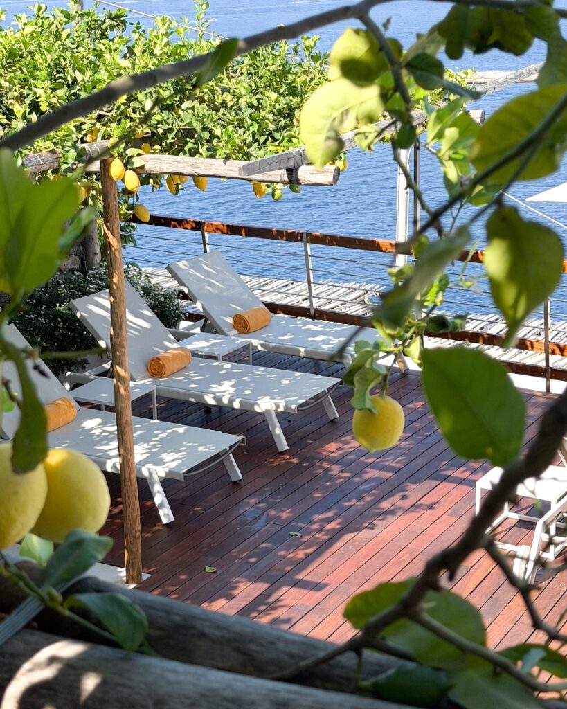 Deck de madeira sob pergolado de limoeiros com espreguiçadeiras no hotel Casa Angelina em Praiano.