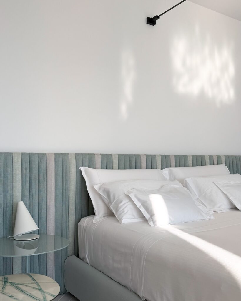 Cabeceira canelada em tons suaves e enxoval branco de alta costura no quarto do hotel Casa Angelina.